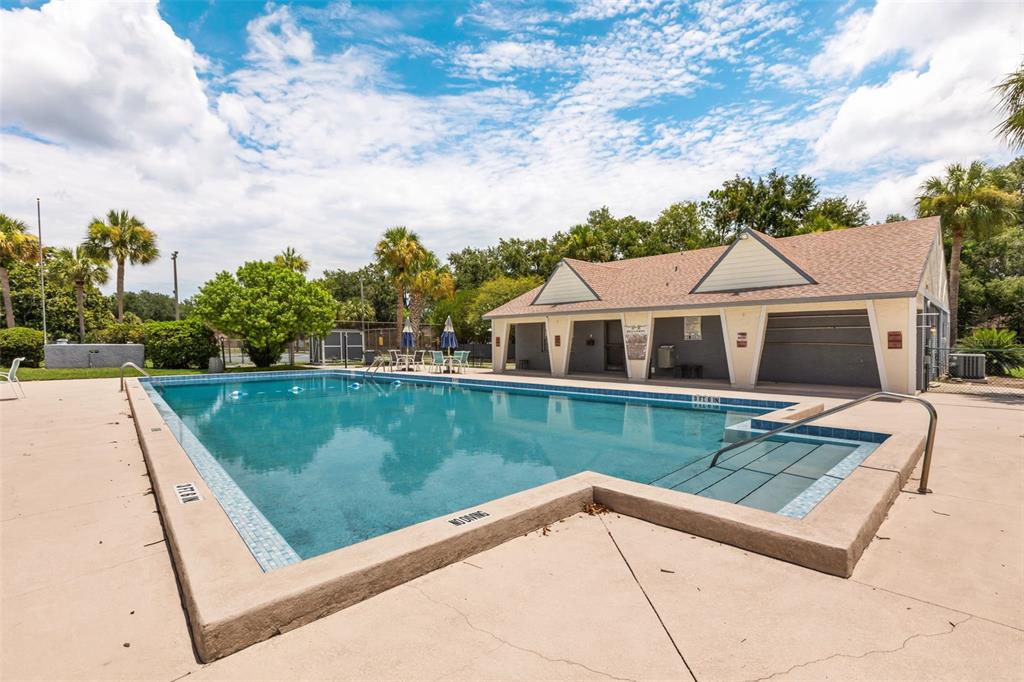 A rectangular swimming pool with a shallow entry area sits beside a community clubhouse building — 4740 AVON COURT UNIT 4740, ST CLOUD, FL