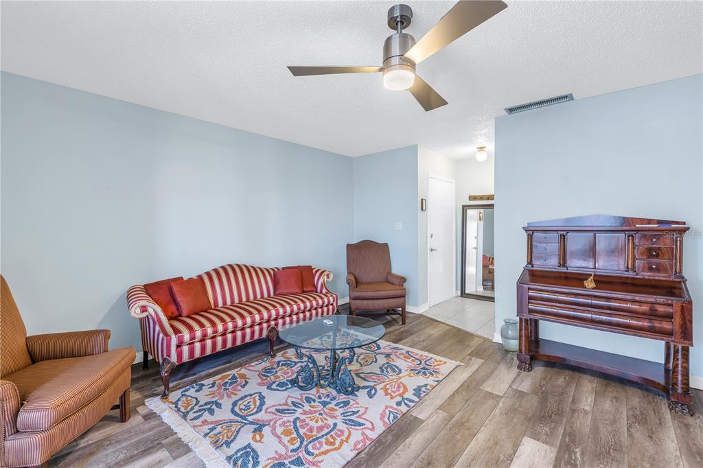 A living room features light blue walls, wood-look flooring, a striped sofa, and a ceiling fan — 4115 34TH WAY S UNIT 195, ST PETERSBURG, FL