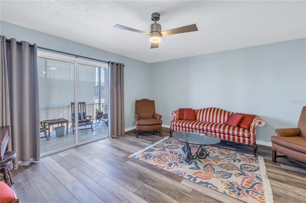 A living room features light blue walls, wood-look flooring, a striped sofa, and sliding glass doors — 4115 34TH WAY S UNIT 195, ST PETERSBURG, FL
