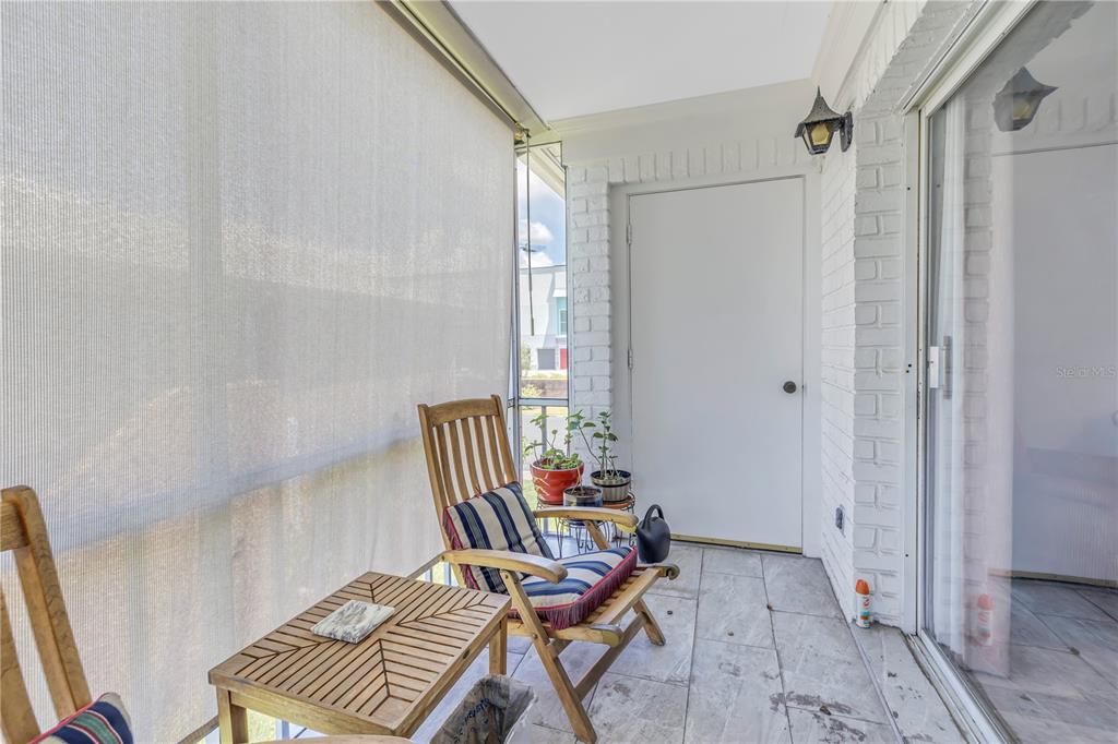 A covered patio features white brick walls, tile flooring, a wooden rocking chair, and screens — 4115 34TH WAY S UNIT 195, ST PETERSBURG, FL