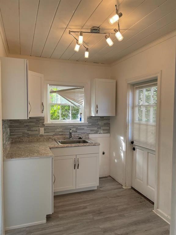 A small kitchen features white cabinets, granite countertops, a tiled backsplash, and a ceiling track light — 104 NE 4th Avenue # C, Delray Beach FL 33483, DELRAY BEACH, FL
