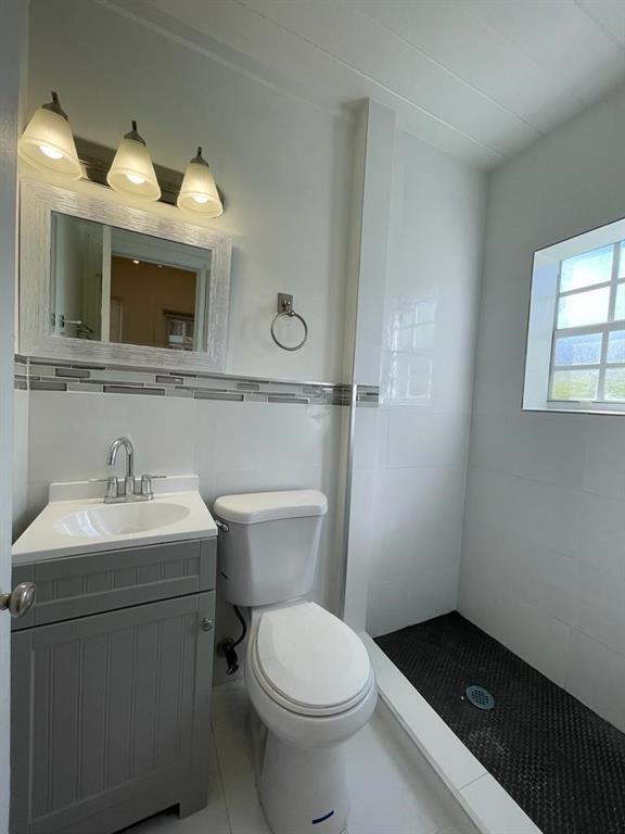 A bathroom features a gray vanity, a white toilet, and a walk-in shower with tile — 104 NE 4th Avenue # C, Delray Beach FL 33483, DELRAY BEACH, FL