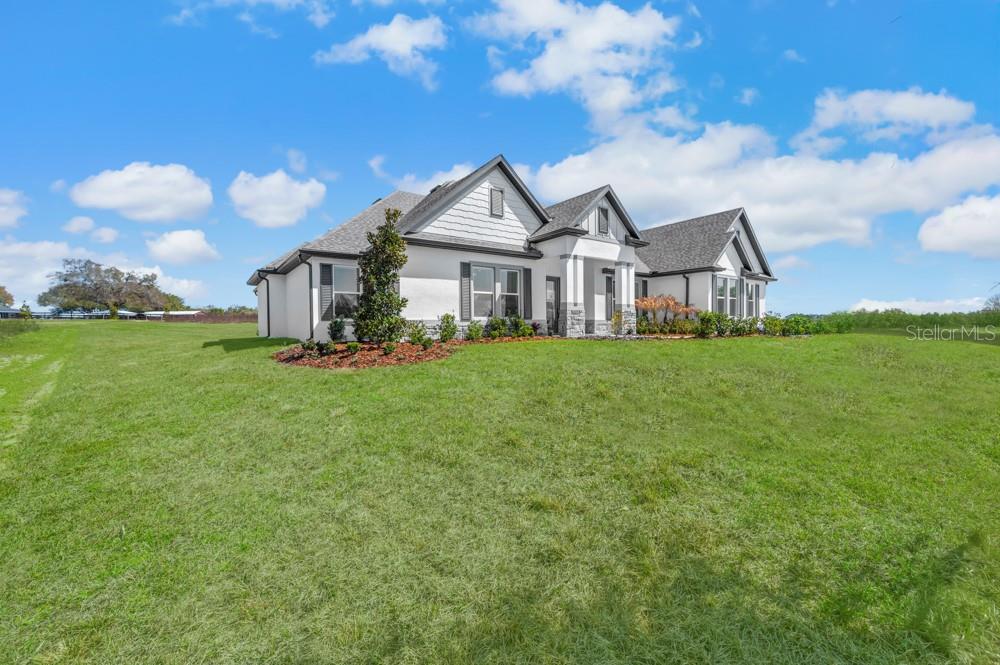 A single-story house with a white exterior, gray roof, and stone accents sits on grass — 3841 SADDLE HILL TRAIL, FRUITLAND PARK, FL
