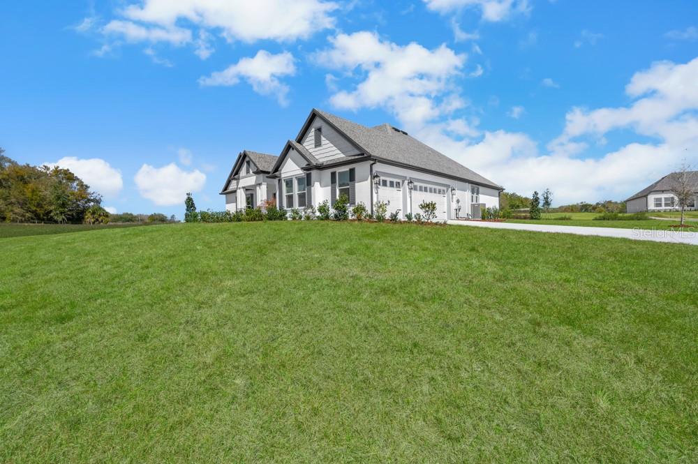 A white single-story house with a gray shingled roof sits on a large grassy hill — 3841 SADDLE HILL TRAIL, FRUITLAND PARK, FL