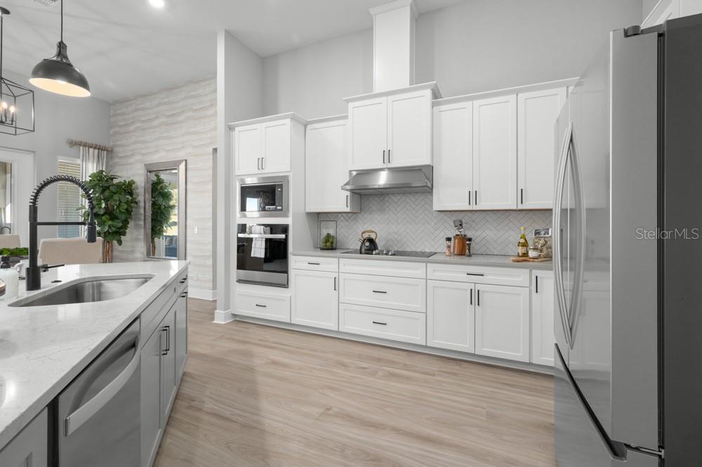 A modern kitchen features white cabinetry, stainless steel appliances, a center island, and light wood flooring — 3841 SADDLE HILL TRAIL, FRUITLAND PARK, FL
