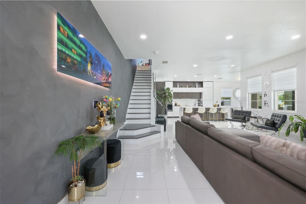 A modern open-concept living room features a gray accent wall, white tile floors, and stairs — 2518 EMPRESS DRIVE, KISSIMMEE, FL
