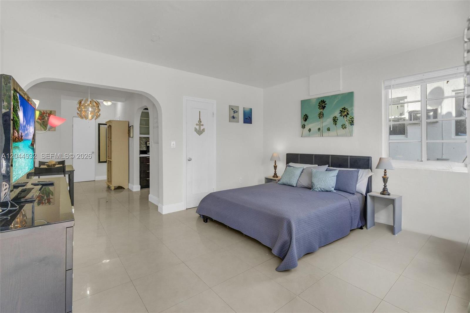 A bedroom with a bed, tile flooring, and an arched entryway leading to another room — 503 75th St # 7504, Miami Beach FL 33141, MIAMI BEACH, FL