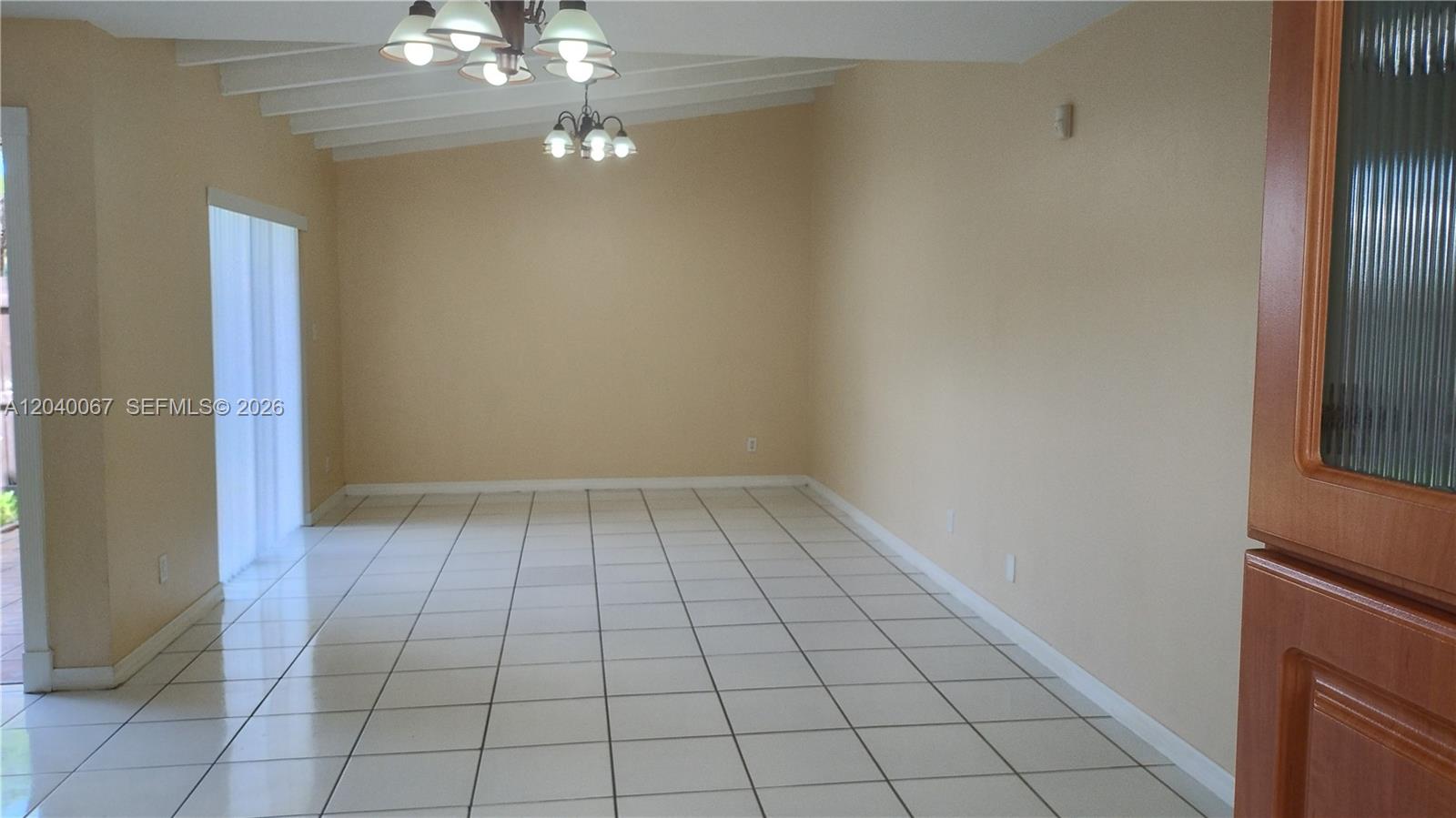 An empty room features white tile flooring, beige walls, and a vaulted ceiling with chandeliers — 7115 SW 111th Pl # 0, Miami FL 33173, MIAMI, FL