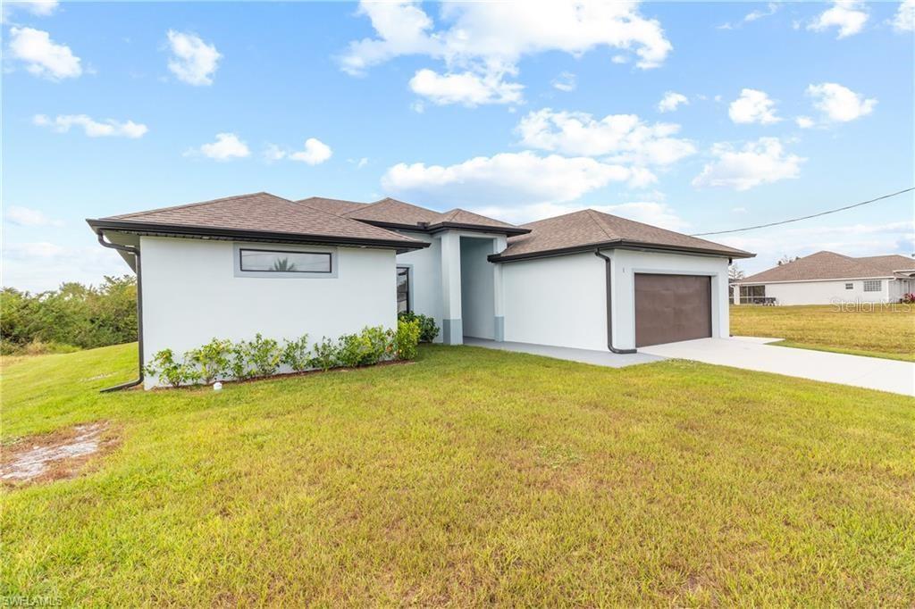 A single-story house with a white exterior, a brown garage door, and a grassy yard — 1806 NE 21ST PLACE, CAPE CORAL, FL
