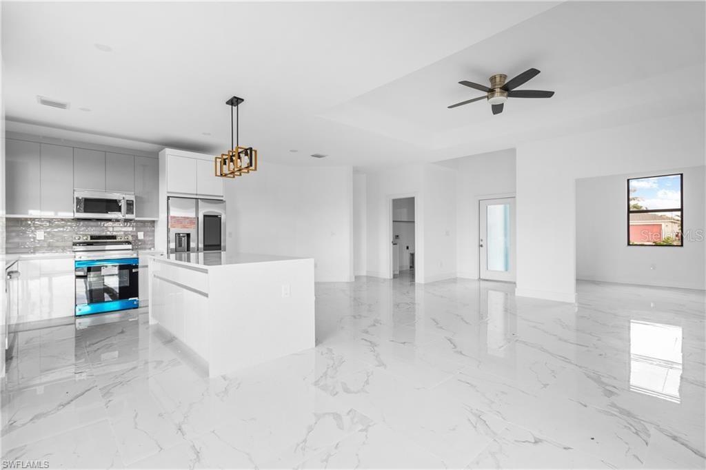 A modern kitchen with white cabinetry and an island opens into a spacious living area — 1806 NE 21ST PLACE, CAPE CORAL, FL