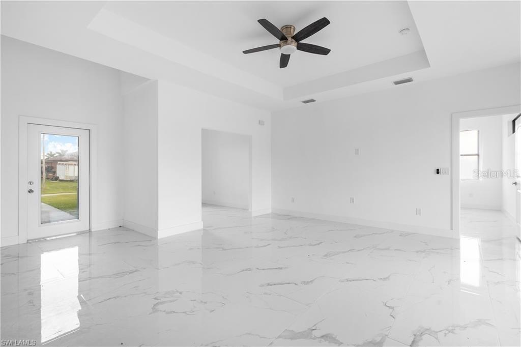 A bright, empty room features white walls, a tray ceiling with a fan, and marble-patterned flooring — 1806 NE 21ST PLACE, CAPE CORAL, FL