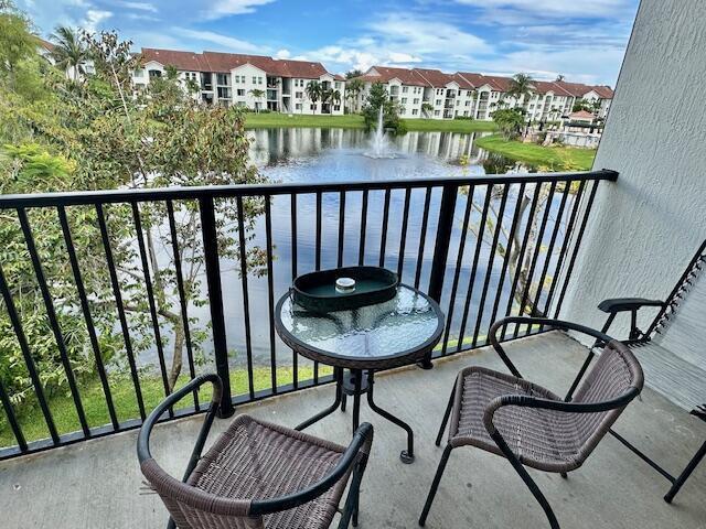 A balcony with two wicker chairs and a glass table overlooks a pond and apartments — 822 Villa Circle, Boynton Beach FL 33435, BOYNTON BEACH, FL