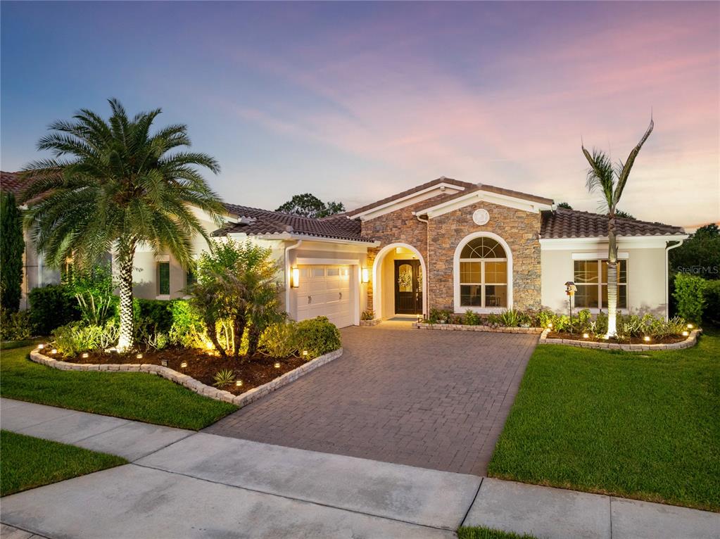A single-story house with a stone facade, tile roof, and a paved driveway at dusk — 13391 ALDERLEY DRIVE, ORLANDO, FL