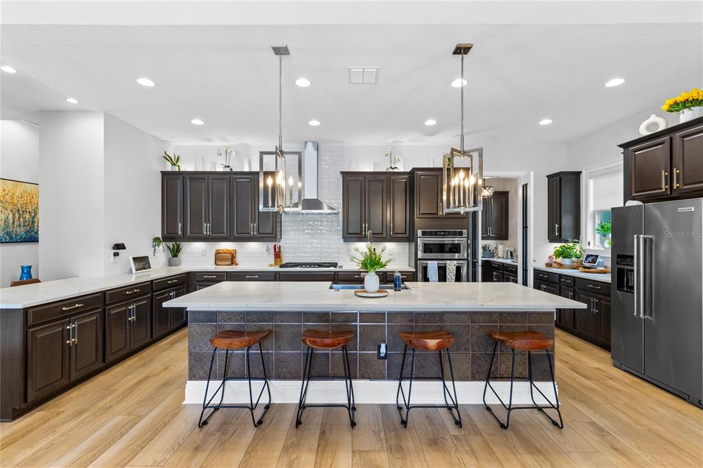 A kitchen features dark wood cabinets, a large central island with seating, and light countertops — 13391 ALDERLEY DRIVE, ORLANDO, FL