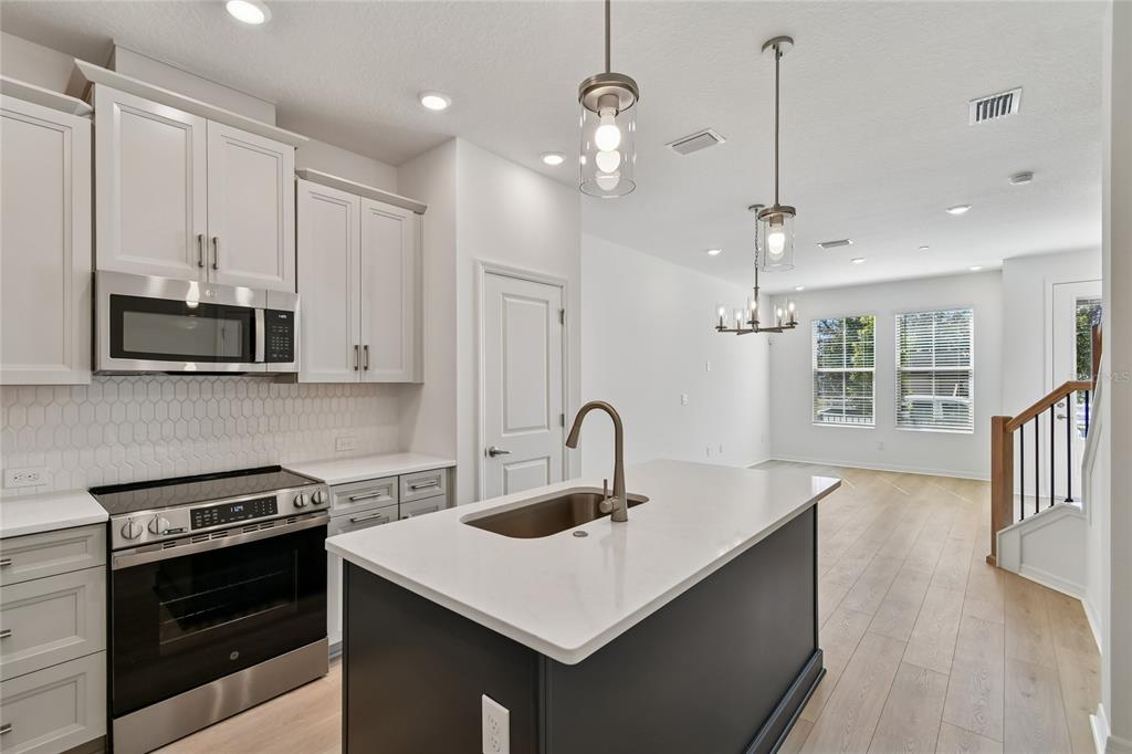 A modern kitchen features a dark island, white cabinetry, stainless steel appliances, and wood flooring — 4333 ROUSH AVENUE, ORLANDO, FL