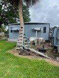 A mobile home exterior with a ladder leaning against a palm tree in the yard — 137 Imperial Way, Fort Pierce FL 34951, FORT PIERCE, FL