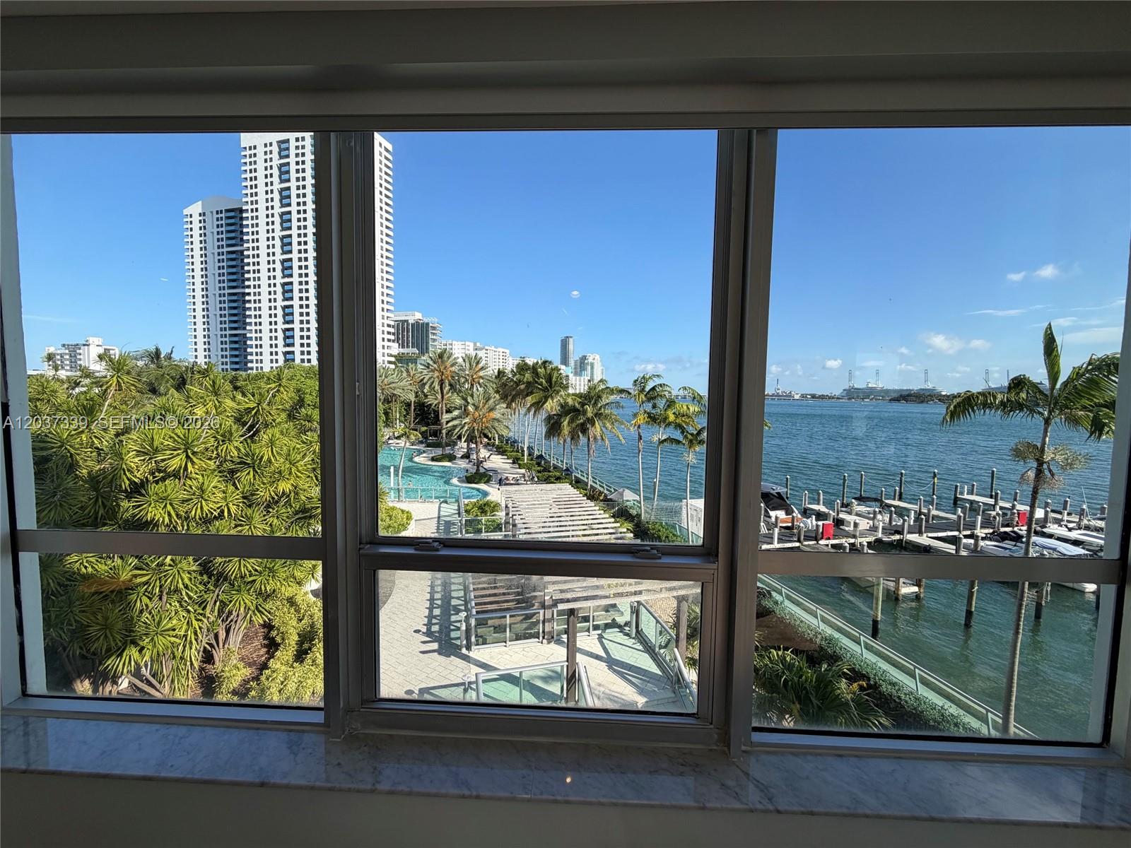 A view from a window shows a pool, palm trees, a marina, and high-rise buildings — 1500 Bay Rd # 338S, Miami Beach FL 33139, MIAMI BEACH, FL