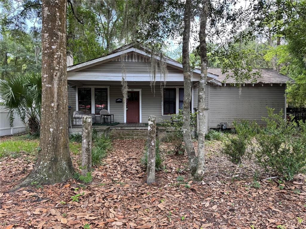 A single-story house with gray horizontal siding and a front porch sits among trees — 907 NW 11TH AVENUE, GAINESVILLE, FL