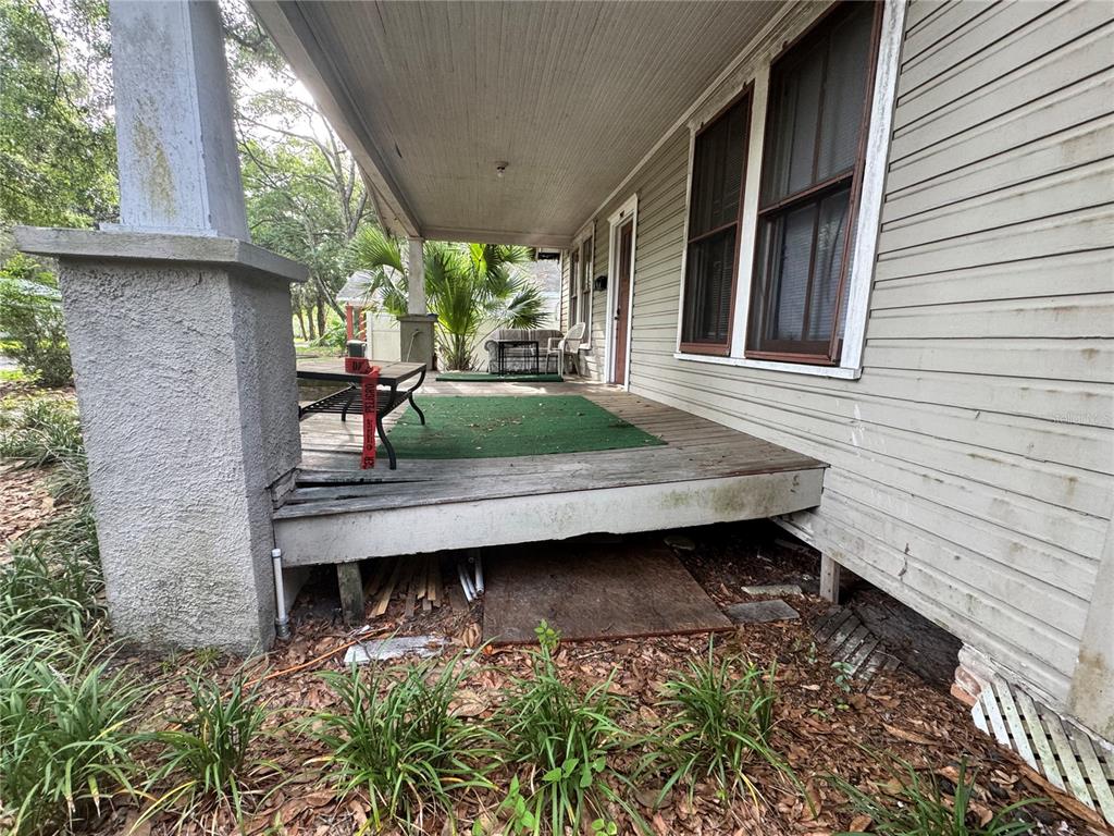 A weathered wooden front porch with a green outdoor rug and a concrete support pillar — 907 NW 11TH AVENUE, GAINESVILLE, FL