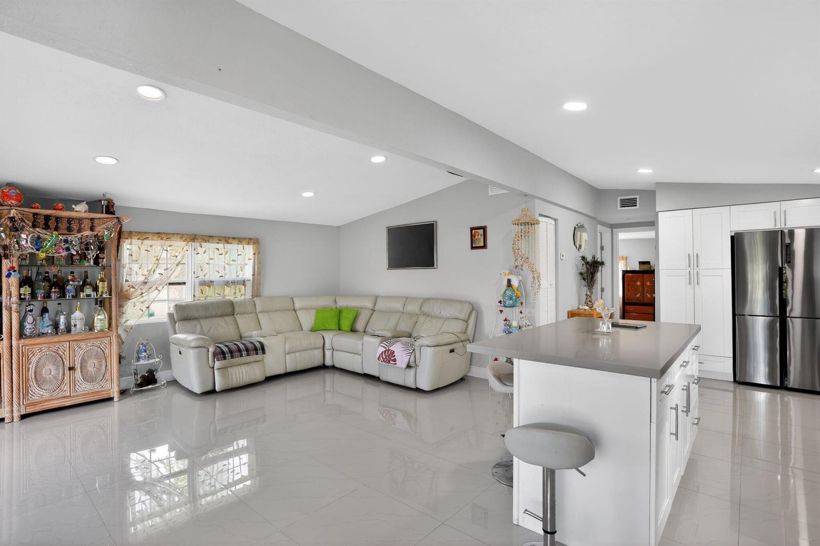 A bright, open-concept living room and kitchen featuring white cabinetry, tile flooring, and a sectional — 27910 Porgie Path, FL 33042, FL