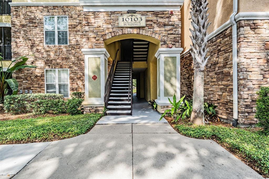 The exterior view shows a stone-faced apartment building entrance with a concrete staircase — 10103 COURTNEY OAKS CIRCLE UNIT 103, TAMPA, FL