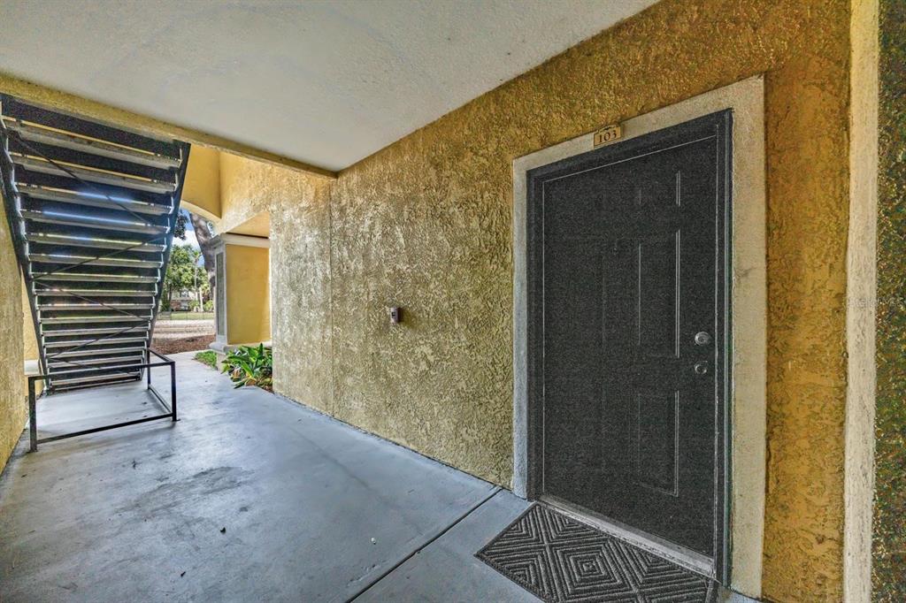 A dark front door with number 103 sits on a concrete walkway beside outdoor stairs — 10103 COURTNEY OAKS CIRCLE UNIT 103, TAMPA, FL