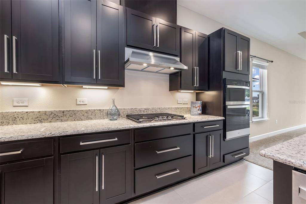 A kitchen features dark wood cabinets, granite countertops, stainless steel appliances, and a gas cooktop — 6 FALMOUTH DRIVE, PALM COAST, FL