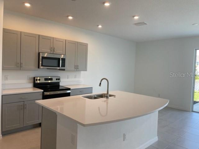 A modern kitchen features gray cabinets, a kitchen island with a sink, and stainless appliances — 5776 HAVEN TERRACE, NOKOMIS, FL
