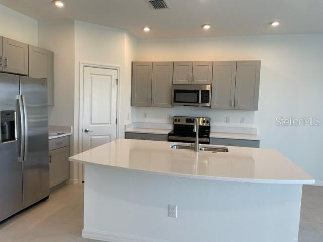 A modern kitchen features gray cabinets, stainless steel appliances, and a large white island — 5776 HAVEN TERRACE, NOKOMIS, FL