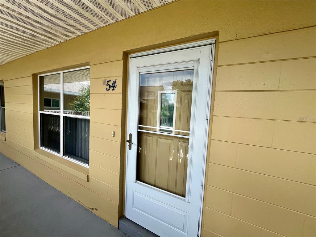 A yellow exterior wall features a white front door and a window at unit 54 — 2220 SPANISH DRIVE UNIT 54, CLEARWATER, FL