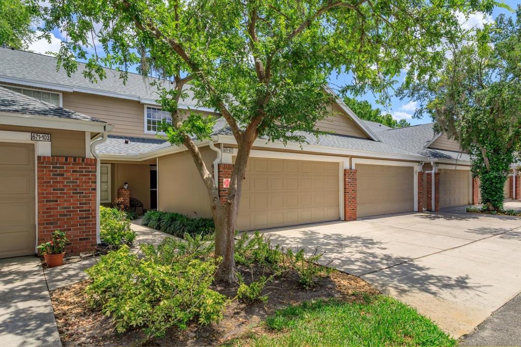 A tan townhouse exterior features brick accents, multiple garage doors, and a small front garden — 671 POST OAK CIRCLE UNIT 107, ALTAMONTE SPRINGS, FL