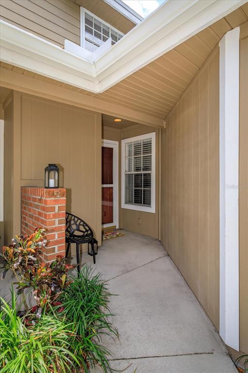 A concrete walkway leads to a covered front porch with a brick pillar and chair — 671 POST OAK CIRCLE UNIT 107, ALTAMONTE SPRINGS, FL