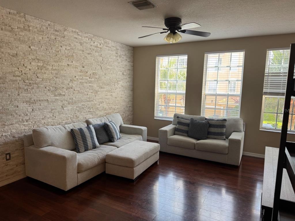 A living room features a textured stone accent wall, light-colored sofas, and dark wood flooring — 3133 BAYSHORE OAKS DRIVE, TAMPA, FL