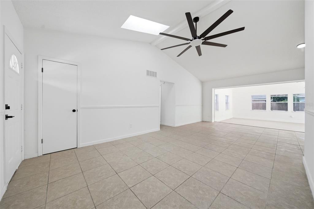 A bright living room features white walls, tile flooring, a vaulted ceiling, and a skylight — 6113 BEAUMONT AVENUE, ORLANDO, FL