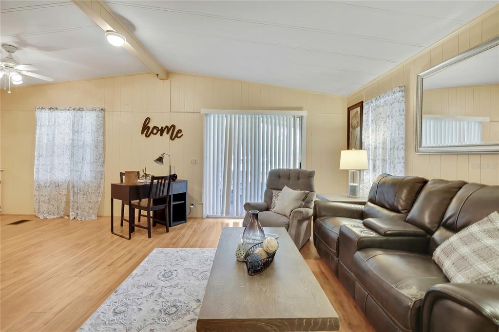 A living room features wood-look flooring, a brown leather sofa, and a small desk area — 57 N BOBWHITE ROAD, WILDWOOD, FL