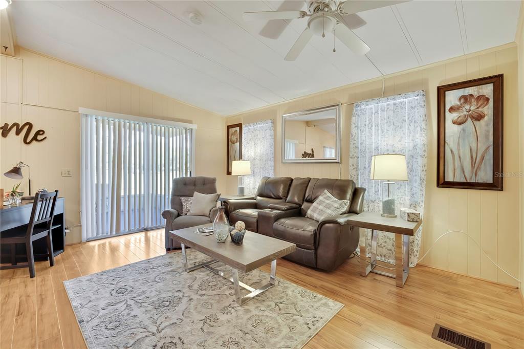 A living room features wood-look flooring, a brown leather sofa, a recliner, and sliding glass doors — 57 N BOBWHITE ROAD, WILDWOOD, FL