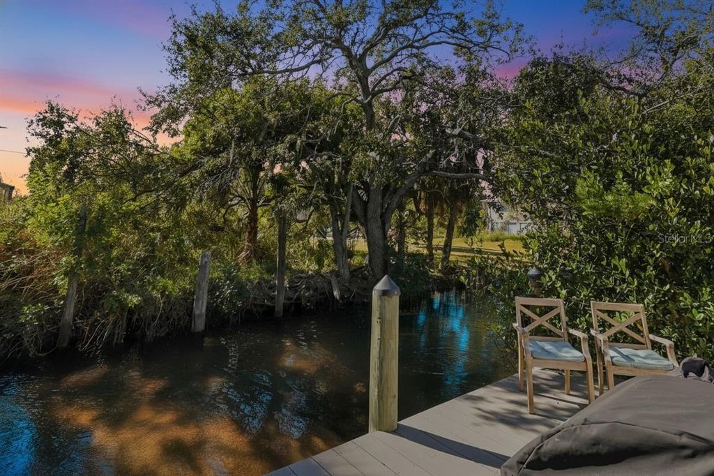 A wooden dock with two chairs overlooks a narrow canal surrounded by lush trees — 27 MICHIANA DRIVE, TERRA CEIA, FL
