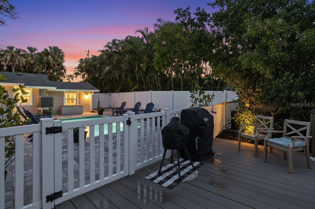 A backyard deck with a grill and chairs overlooks a swimming pool at sunset — 27 MICHIANA DRIVE, TERRA CEIA, FL