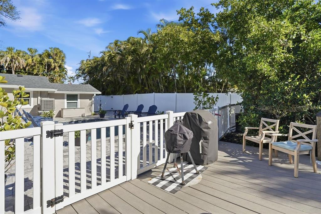 A backyard deck features a grill, outdoor seating, and a white fence enclosing a pool area — 27 MICHIANA DRIVE, TERRA CEIA, FL