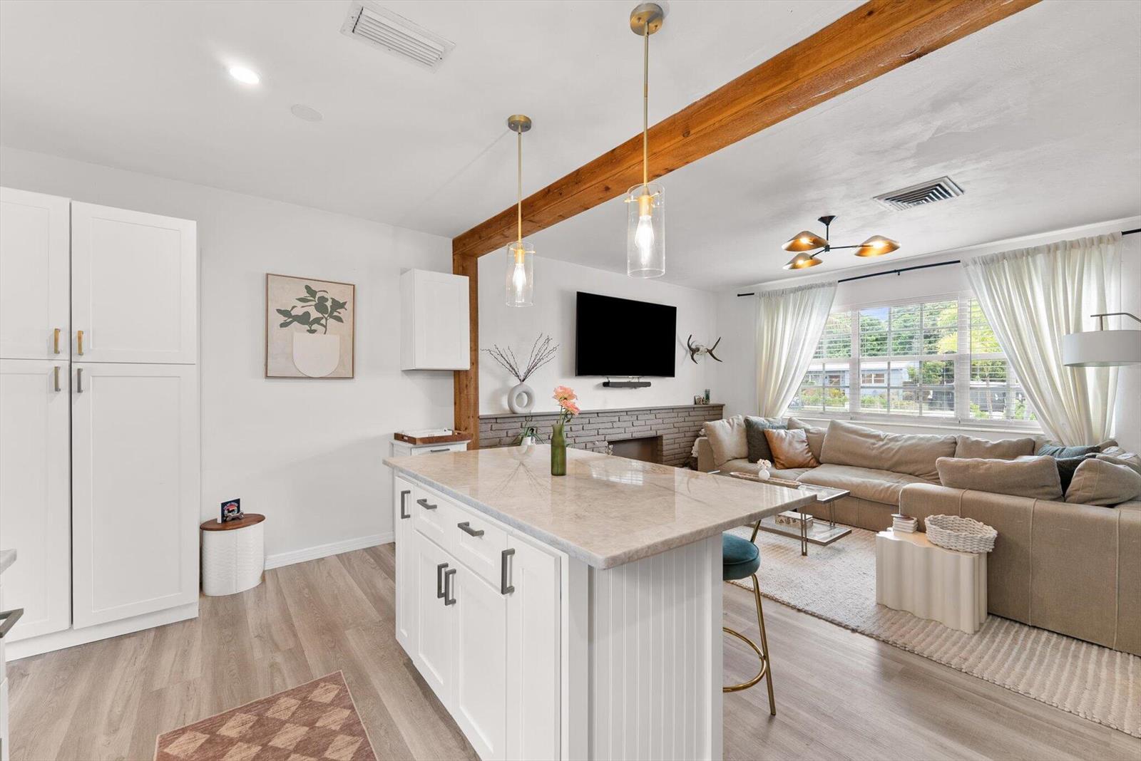 An open-concept kitchen with a stone island overlooks a living room with a brick fireplace — 350 Forest Hill Boulevard, West Palm Beach FL 33405, WEST PALM BEACH, FL