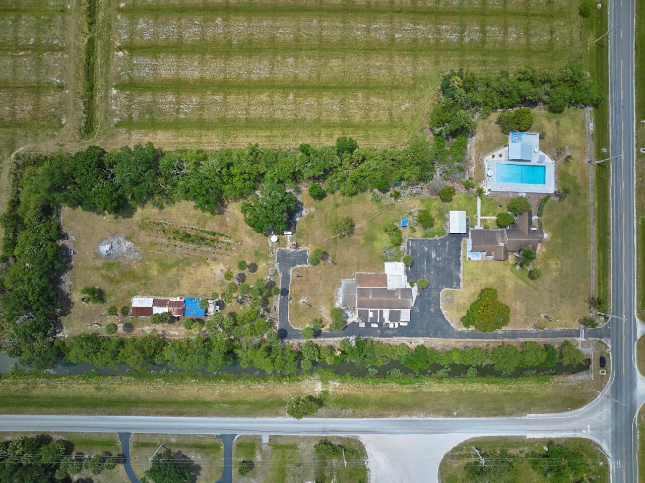 An aerial view shows a residential property with a house, pool, and outbuildings near fields — 14601 Orange Avenue, Fort Pierce FL 34945, FORT PIERCE, FL