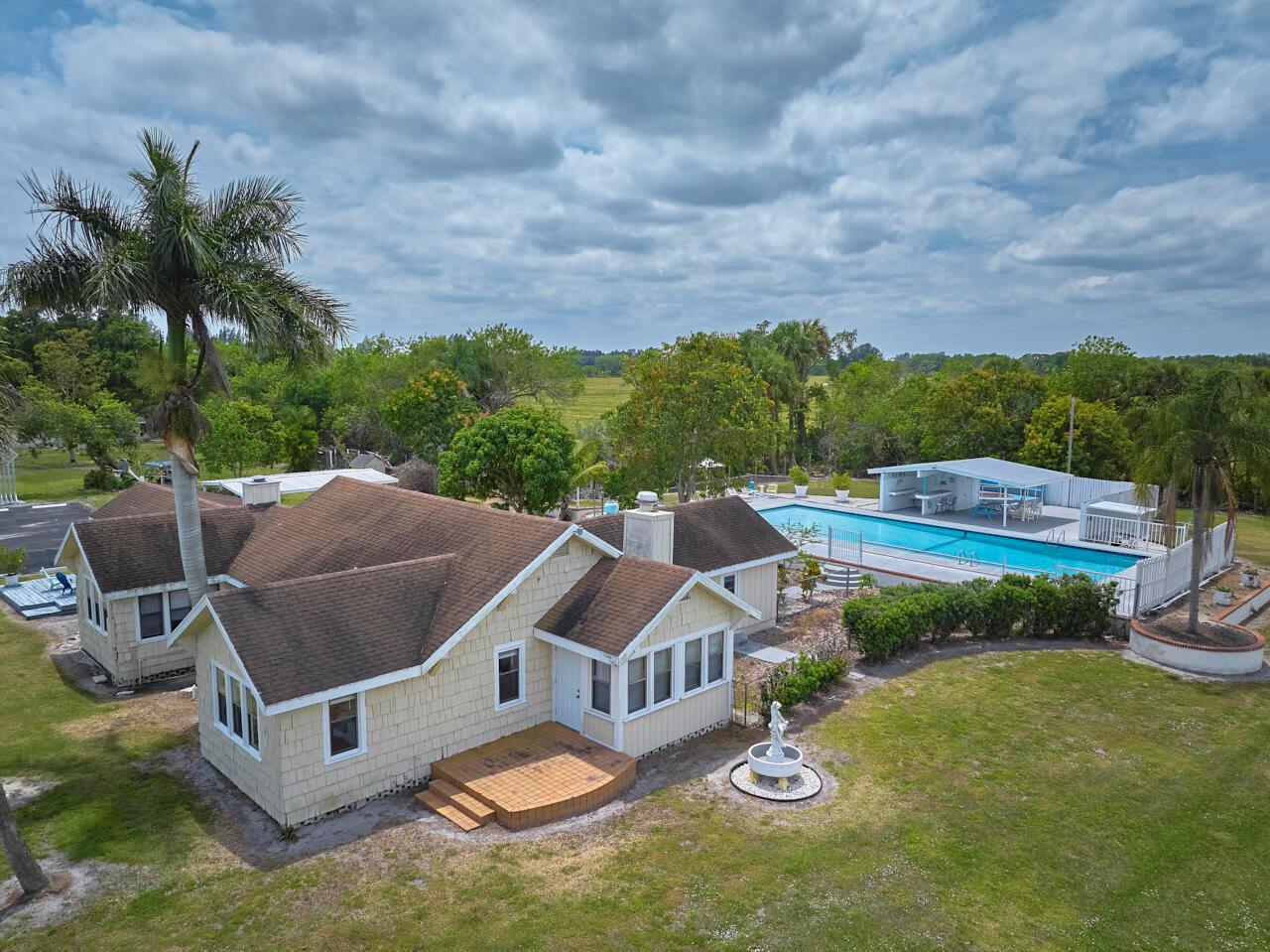 An aerial view of a tan house with a brown roof, pool, and backyard fountain — 14601 Orange Avenue, Fort Pierce FL 34945, FORT PIERCE, FL