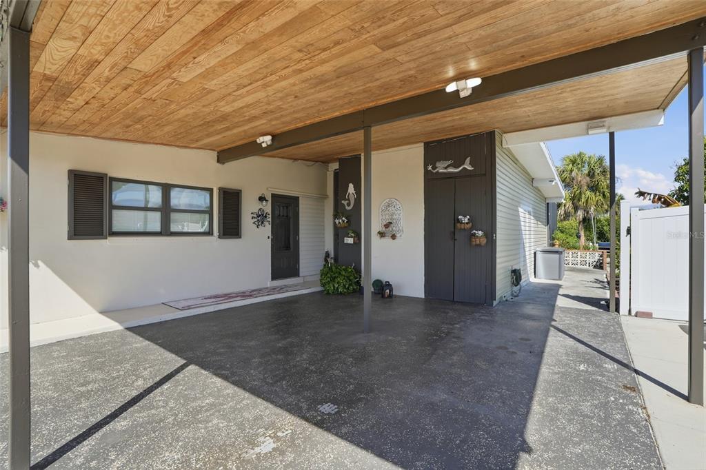A covered carport features a wood-paneled ceiling, a concrete floor, and a dark storage closet — 4086 GARDNER DRIVE, PORT CHARLOTTE, FL