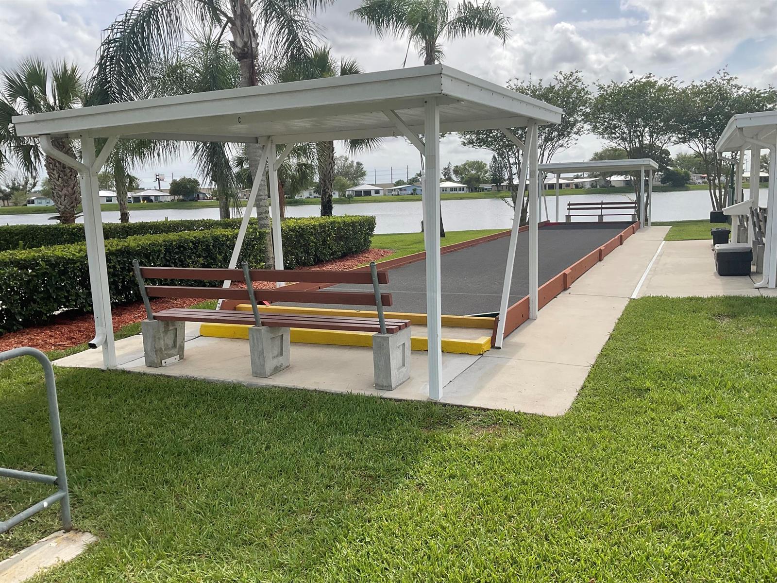 A covered shuffleboard court sits outdoors next to a lake with benches and landscaping — 14151 Cisne Circle, Fort Pierce FL 34951, FORT PIERCE, FL