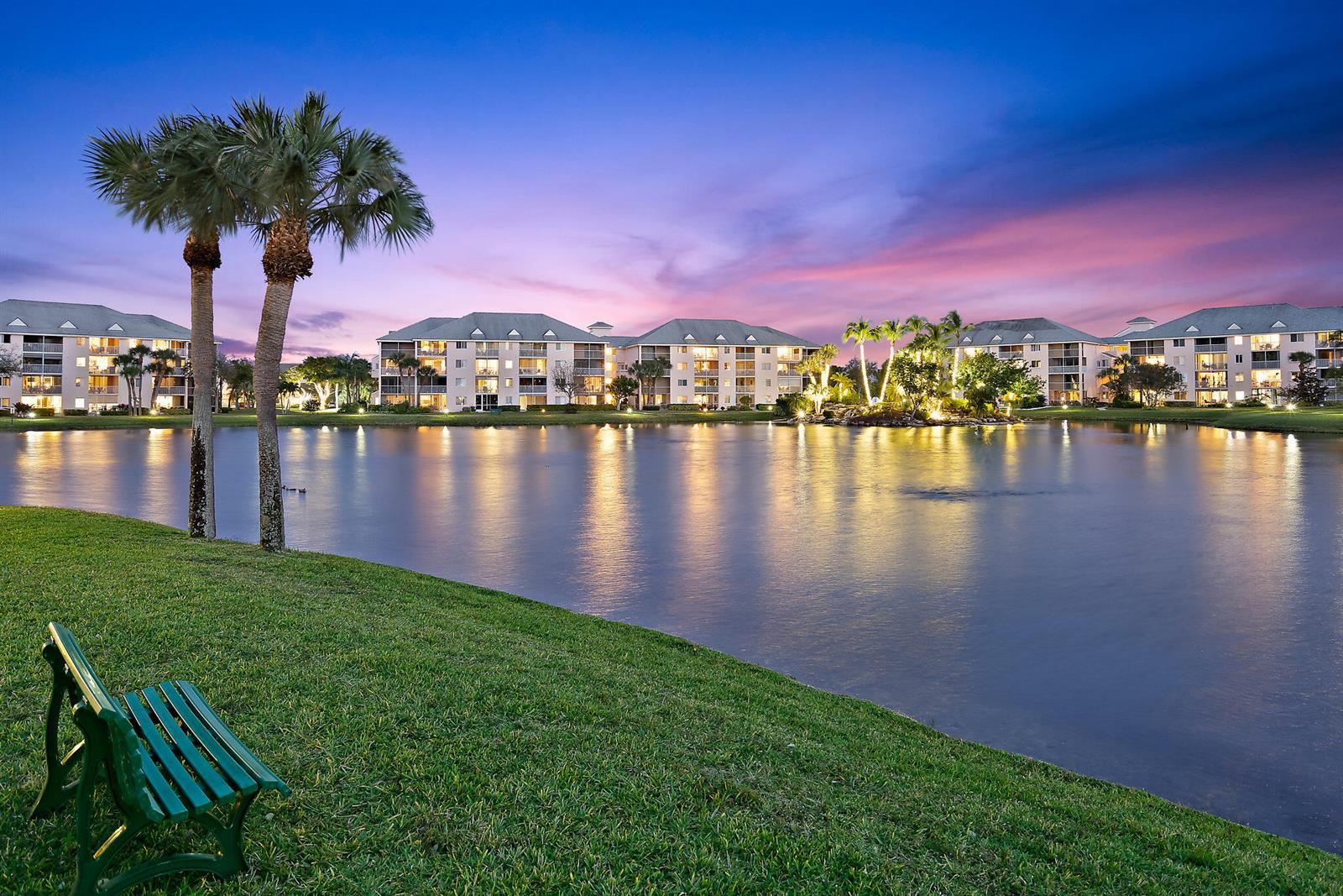 A green bench sits on a grassy lawn overlooking a lake and multi-story apartment buildings — 353 S Us Highway 1 # C203, Jupiter FL 33477, JUPITER, FL