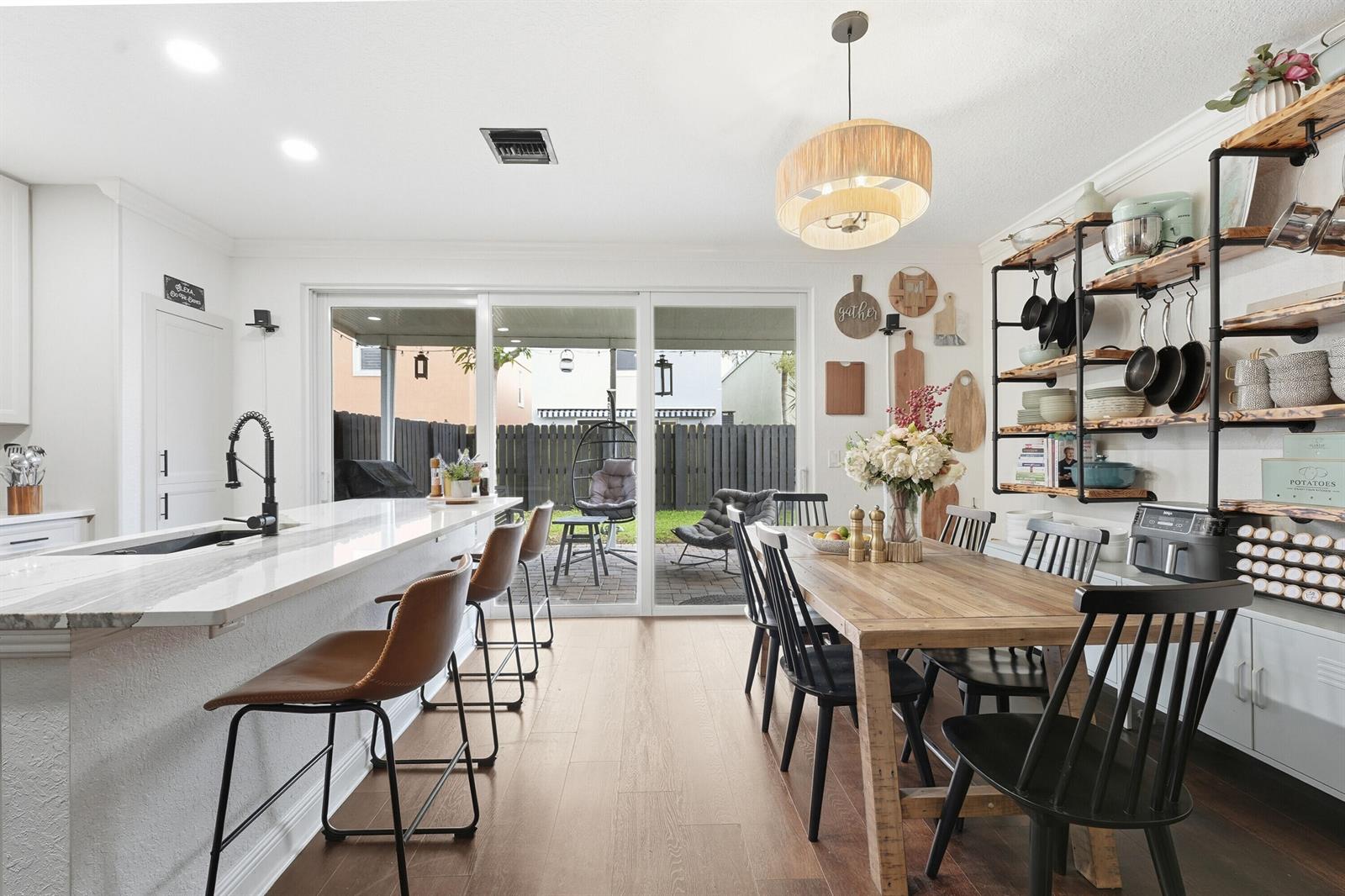 A kitchen and dining area with a breakfast bar, wooden table, and sliding glass doors — 3221 Johns Place, Palm Springs FL 33461, PALM SPRINGS, FL