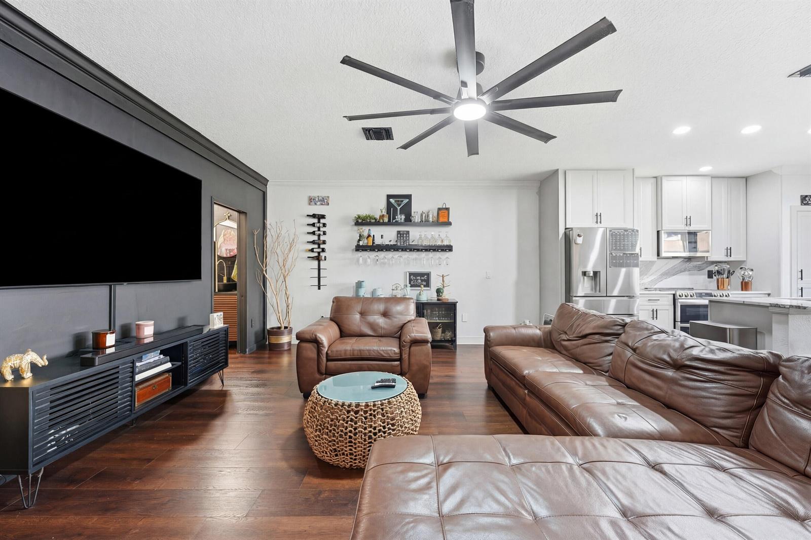A living room features a large television, brown leather furniture, and an open kitchen area — 3221 Johns Place, Palm Springs FL 33461, PALM SPRINGS, FL