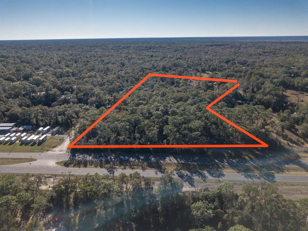 An aerial view shows a wooded plot of land outlined in orange along a road — N US HWY 17, DELAND, FL