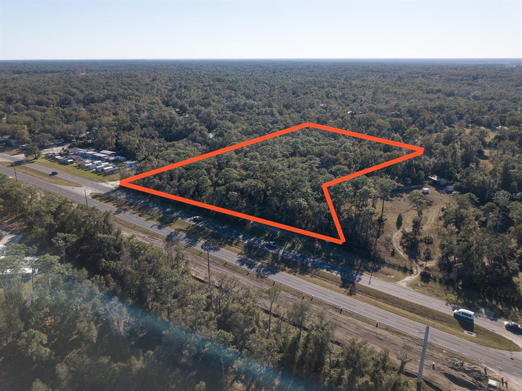 An aerial view shows a wooded plot of land outlined in orange next to a highway — N US HWY 17, DELAND, FL