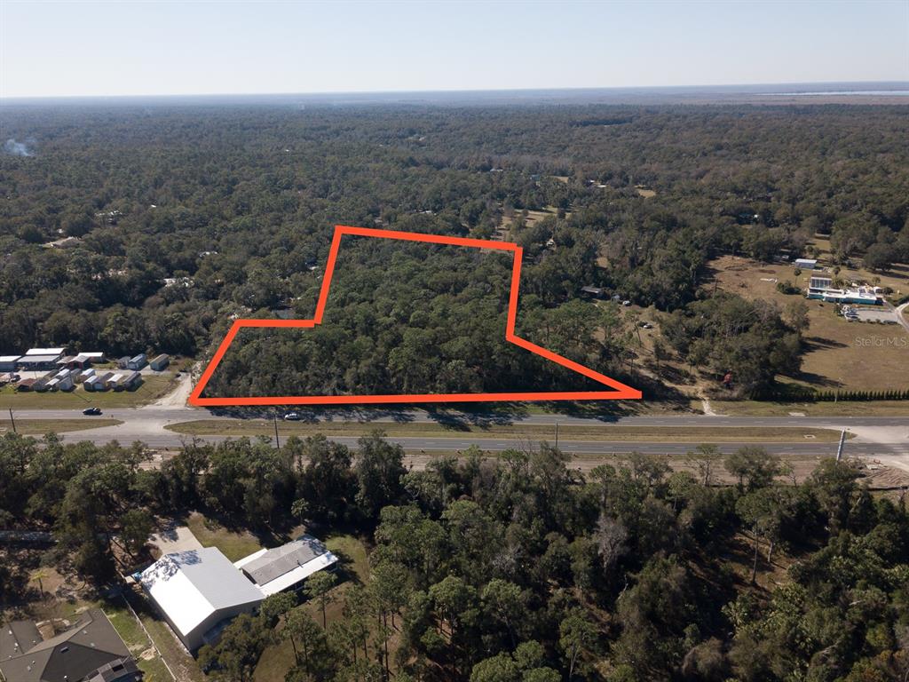 An aerial view shows a wooded plot of land outlined in red along a road — N US HWY 17, DELAND, FL